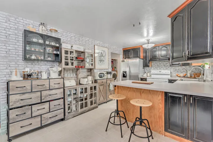 Kitchen featuring a peninsula, light countertops, stainless steel refrigerator with ice dispenser, white electric stove, and a kitchen breakfast bar