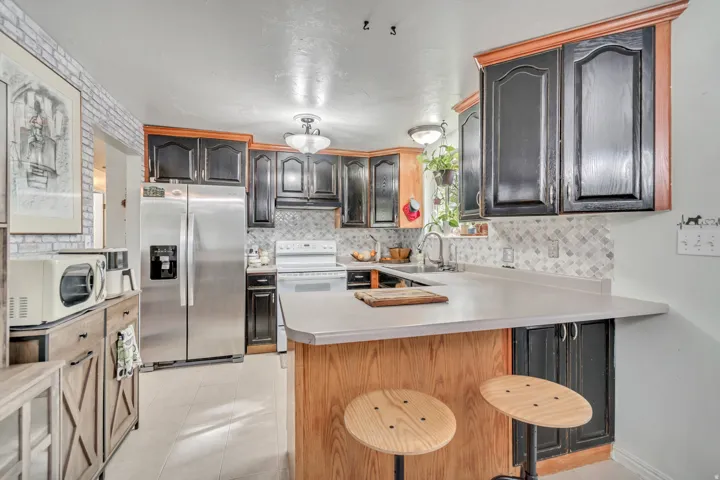 Kitchen featuring light countertops, a peninsula, white appliances, a kitchen bar, and light tile patterned floors