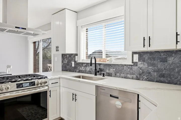 Kitchen with stainless steel appliances, island range hood, white cabinets, light stone counters, and decorative backsplash