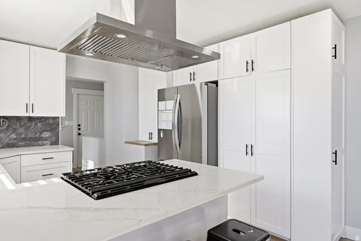 Kitchen with island range hood, light stone countertops, freestanding refrigerator, and white cabinetry
