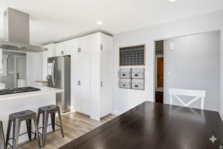 Kitchen with island range hood, light wood finished floors, stainless steel appliances, white cabinets, and a breakfast bar area