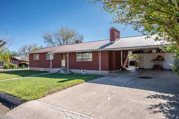 Ranch-style house featuring a metal roof, a front yard, concrete driveway, and a chimney