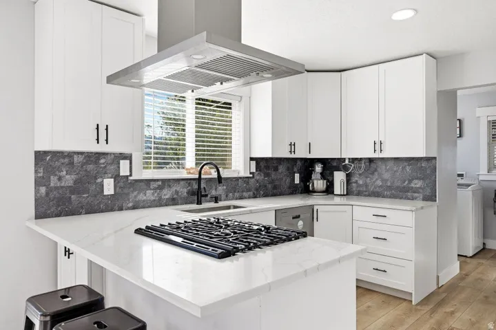 Kitchen with island range hood, light stone counters, white cabinets, light wood-style floors, and recessed lighting