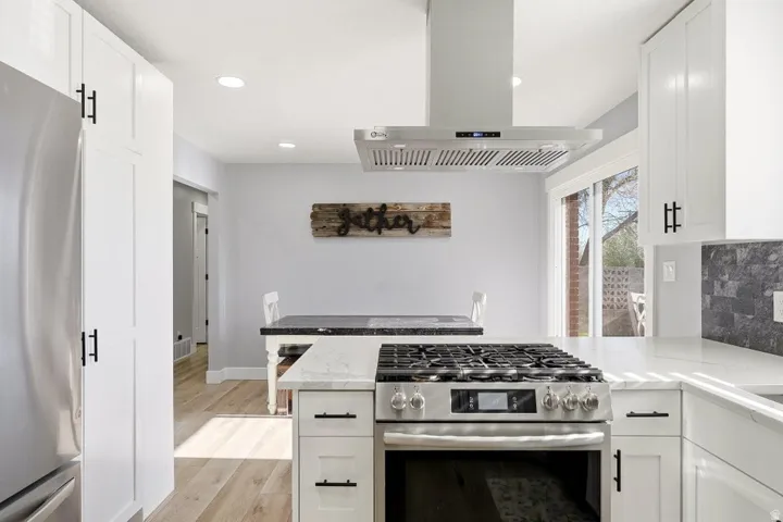 Kitchen with stainless steel appliances, island range hood, white cabinetry, a peninsula, and recessed lighting
