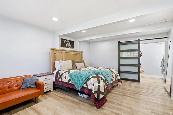 Bedroom with a barn door, light wood-style floors, recessed lighting, and beamed ceiling
