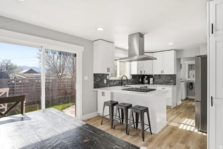 Kitchen with a breakfast bar, a peninsula, white cabinetry, light wood finished floors, and recessed lighting
