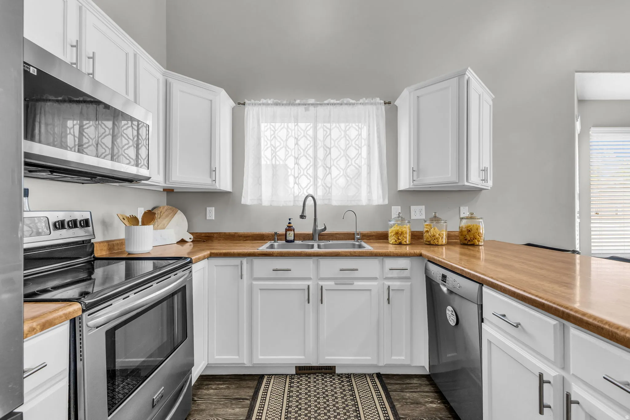 Kitchen with stainless steel appliances, white cabinets, light countertops, and dark wood finished floors