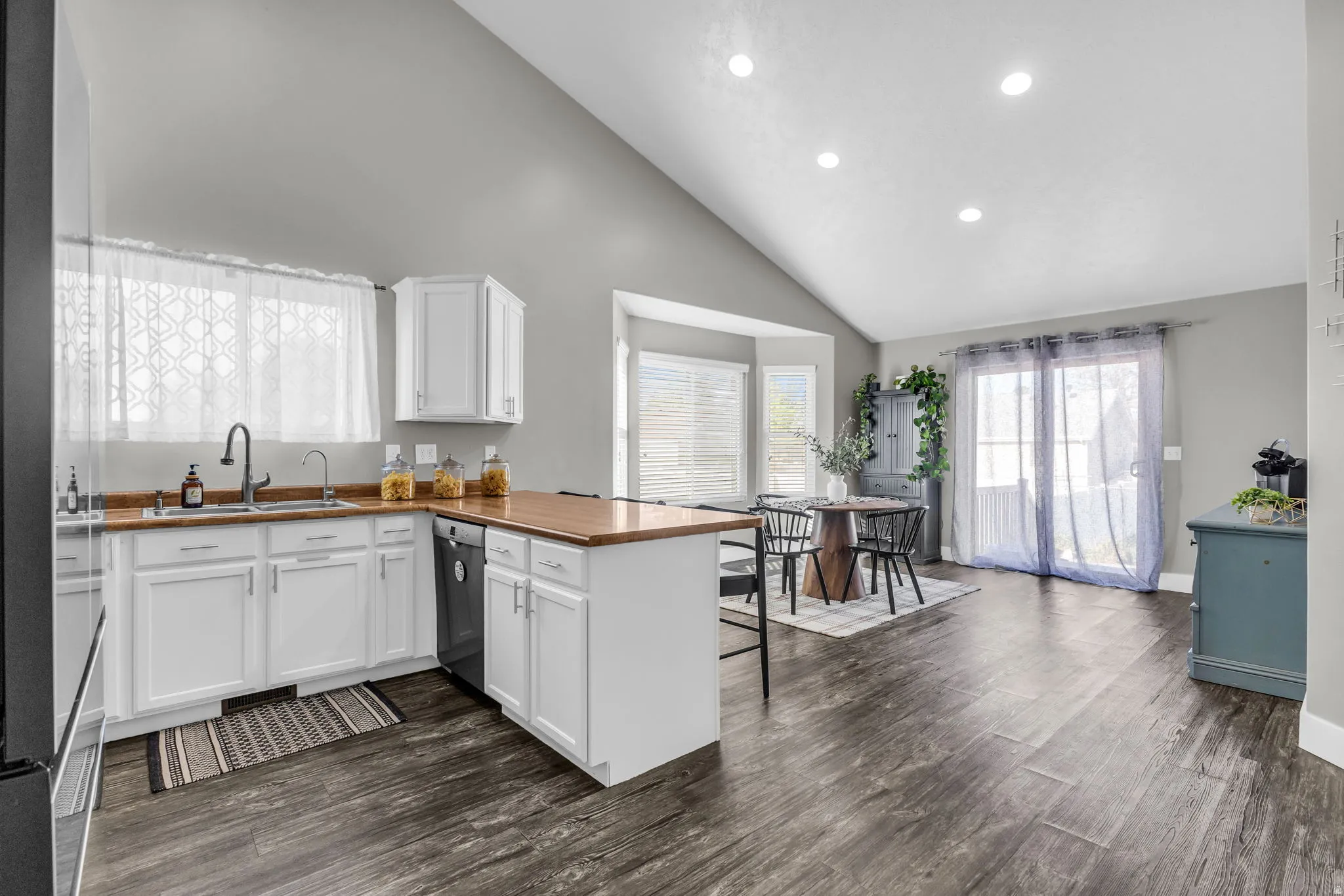 Kitchen with a peninsula, dark wood-style floors, stainless steel appliances, white cabinetry, and vaulted ceiling