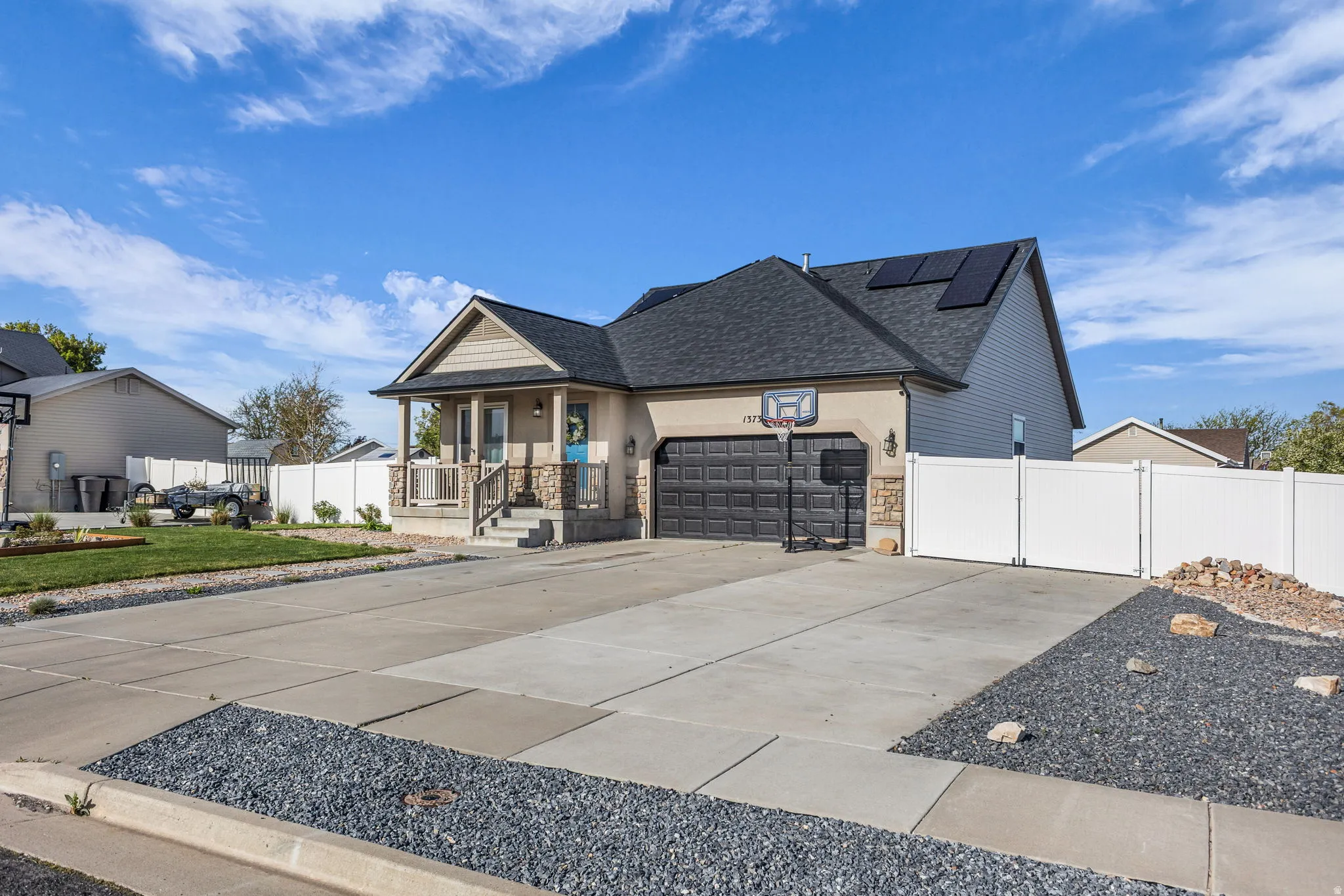 View of front facade with a shingled roof, an attached garage, driveway, a porch, and solar panels