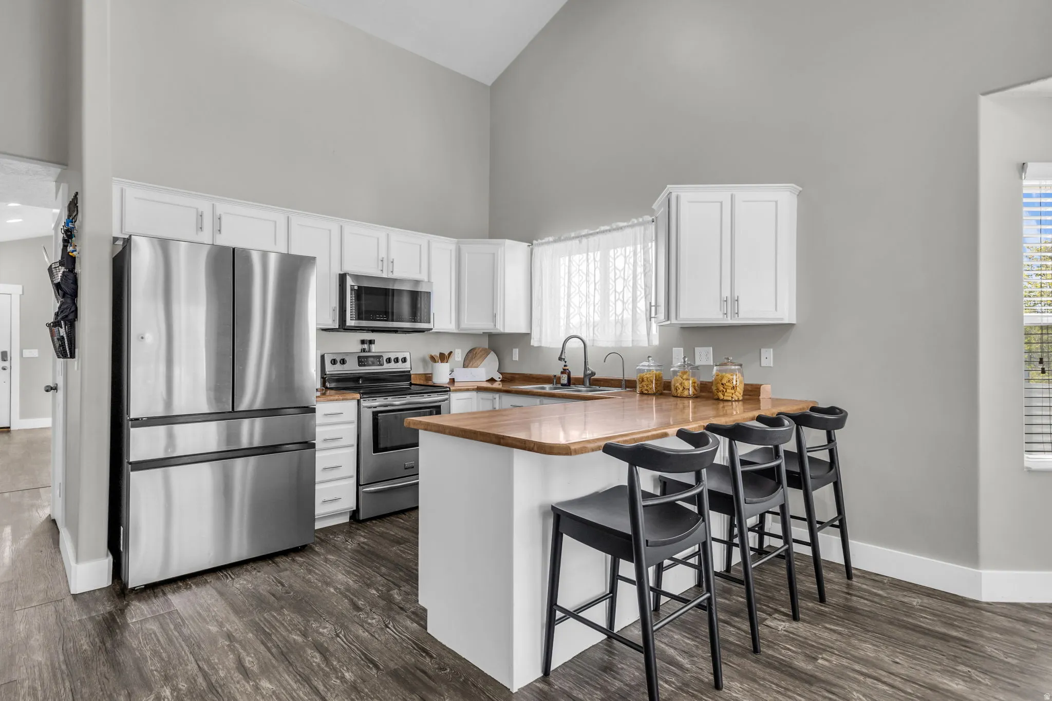 Kitchen with stainless steel appliances, a kitchen bar, a peninsula, white cabinetry, and dark wood-type flooring