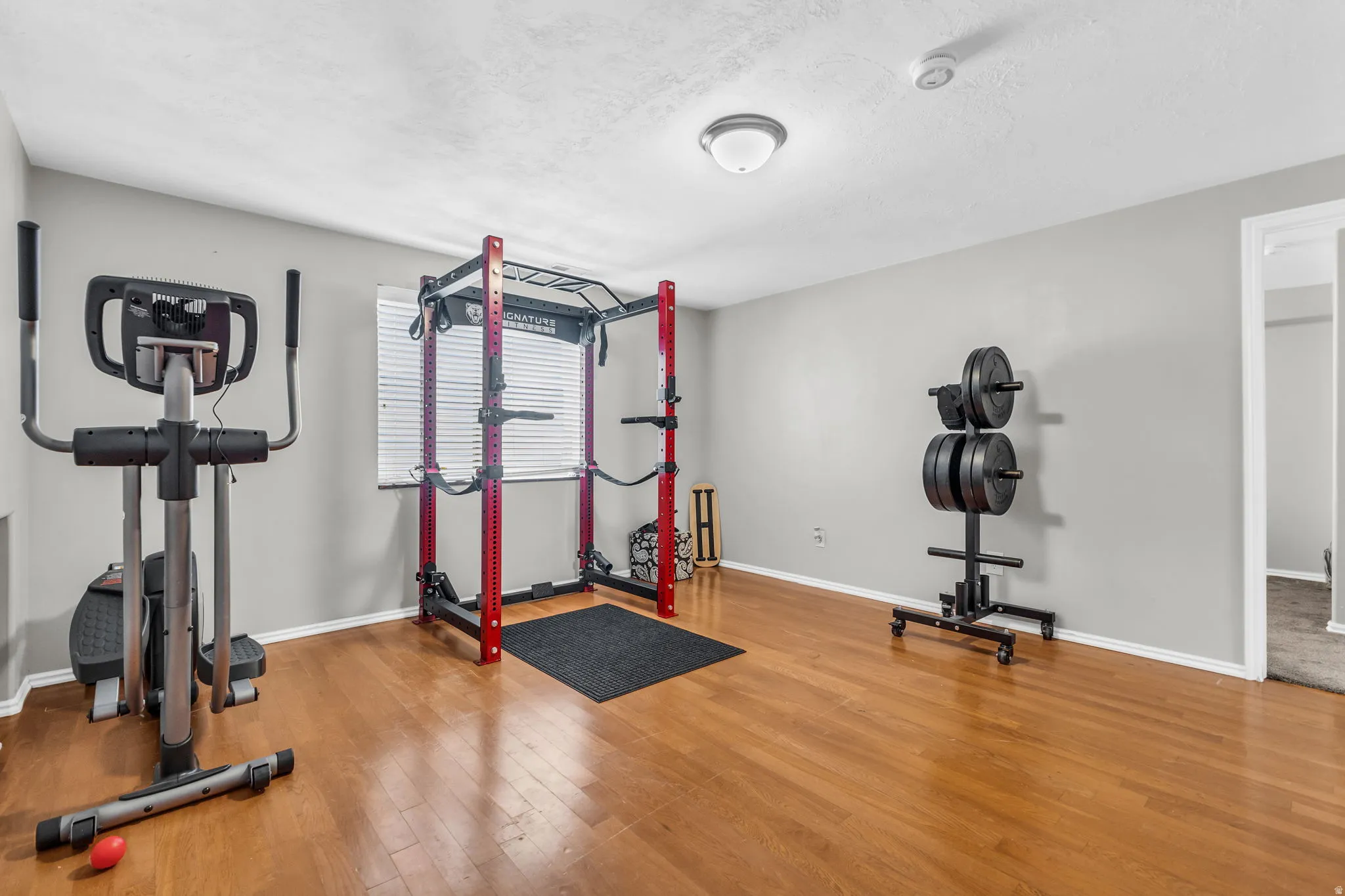 Exercise room with light wood-type flooring and a textured ceiling