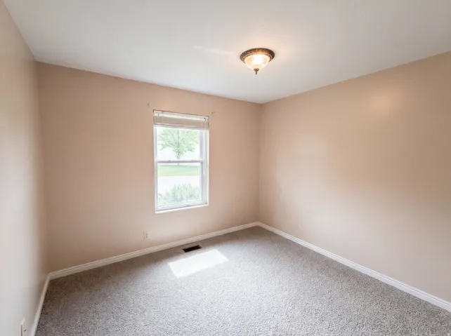 Empty room with light colored carpet and baseboards
