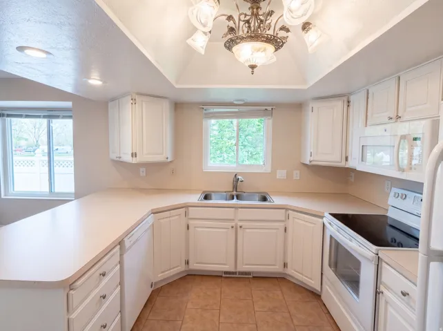 Kitchen featuring white appliances, light countertops, white cabinetry, and a tray ceiling