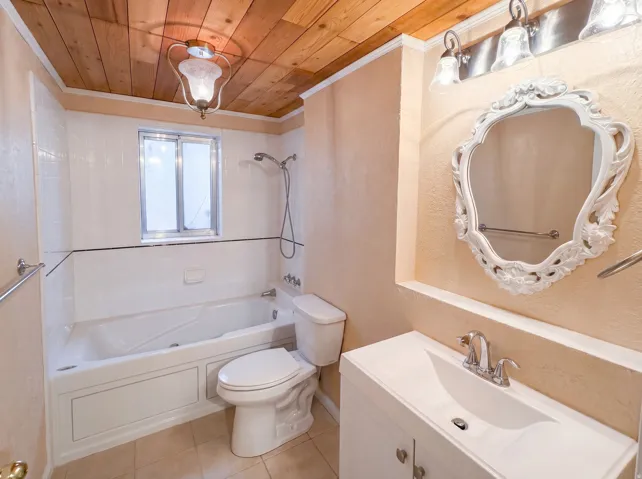 Full bathroom featuring vanity, wooden ceiling,  shower combination, light tile patterned flooring, and crown molding