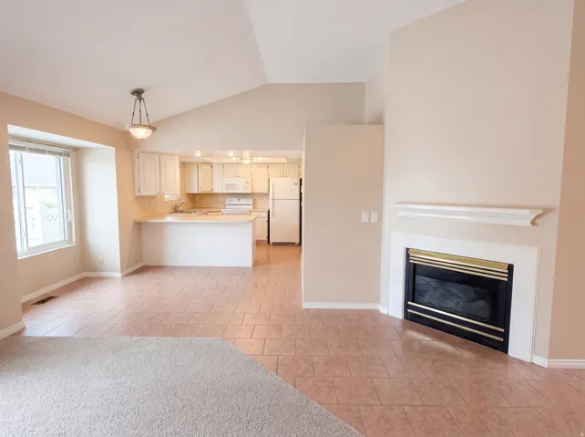 Unfurnished living room featuring lofted ceiling, light tile patterned flooring, and a glass covered fireplace
