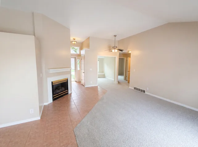 Unfurnished living room featuring a ceiling fan, lofted ceiling, a glass covered fireplace, light colored carpet, and light tile patterned floors