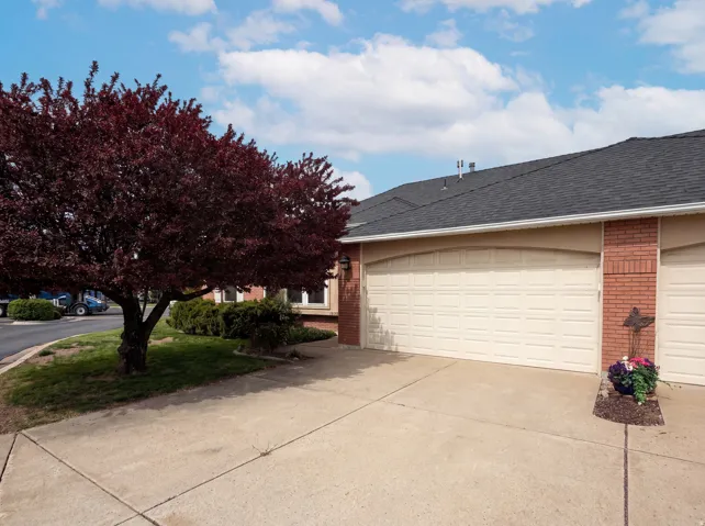 View of side of property with a shingled roof, brick siding, driveway, and an attached garage