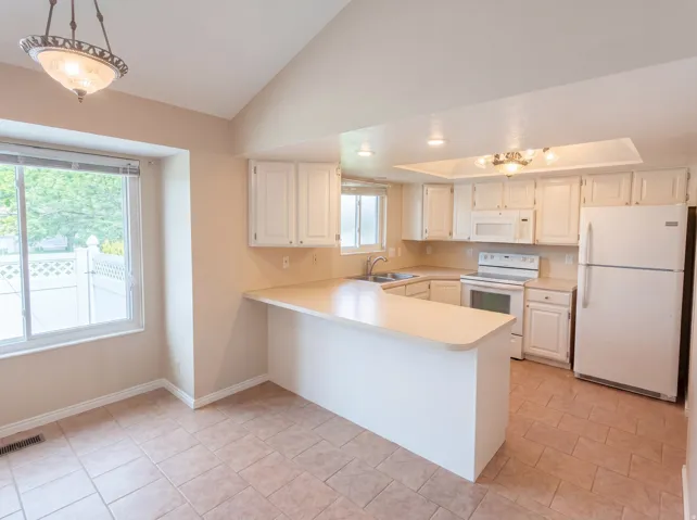 Kitchen featuring light countertops, white appliances, white cabinetry, a peninsula, and vaulted ceiling