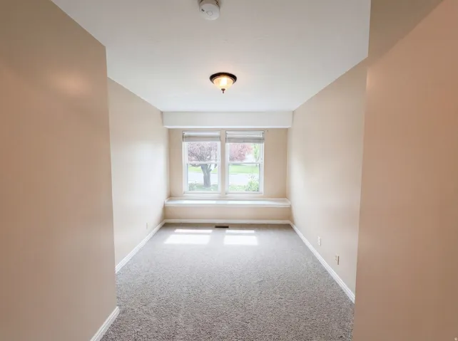 Empty room with light colored carpet and a smoke detector