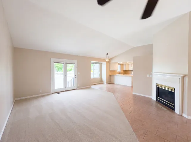 Unfurnished living room featuring ceiling fan, vaulted ceiling, a glass covered fireplace, and light tile patterned flooring