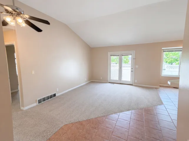Unfurnished room featuring light colored carpet, light tile patterned flooring, a ceiling fan, and lofted ceiling