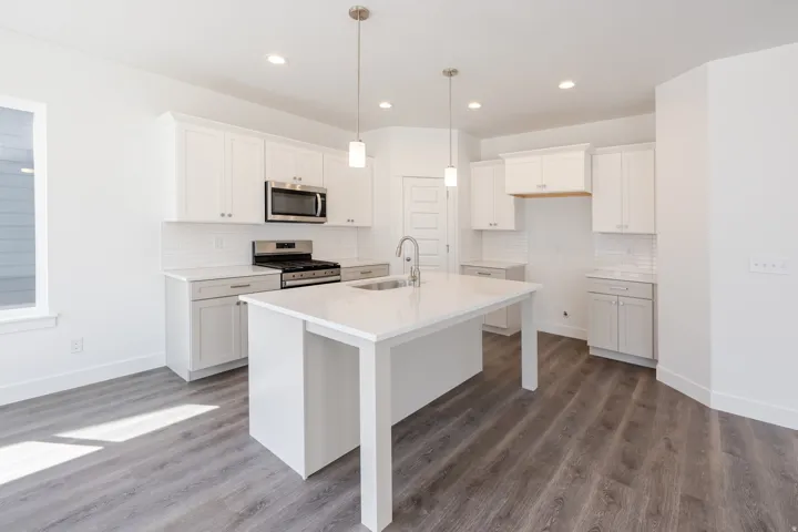 Open-concept kitchen featuring white cabinetry, stainless steel appliances, a center island with sink, and wood-finish flooring