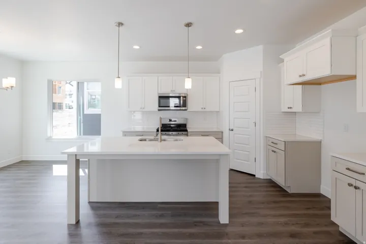 Kitchen featuring an island with sink, white shaker-style cabinetry, stainless steel appliances, and pendant lighting
