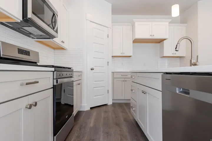 White shaker cabinetry, stainless steel appliances, subway tile backsplash, wood-finish flooring, and a kitchen island with integrated sink