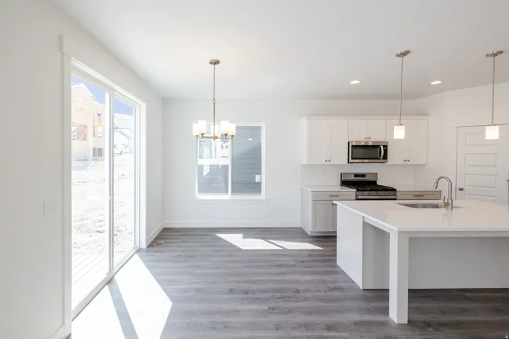 Kitchen and dining area featuring wood-finish flooring, white cabinetry, a kitchen island with integrated sink, stainless steel appliances, and a sliding glass door