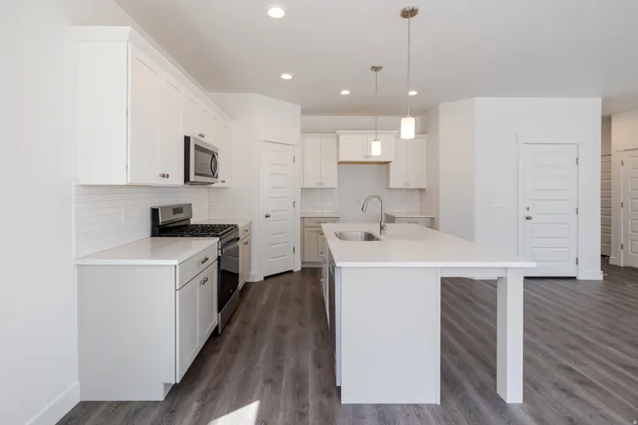 White shaker cabinetry, stainless steel appliances, solid surface countertops, subway tile backsplash, and wood-finish flooring