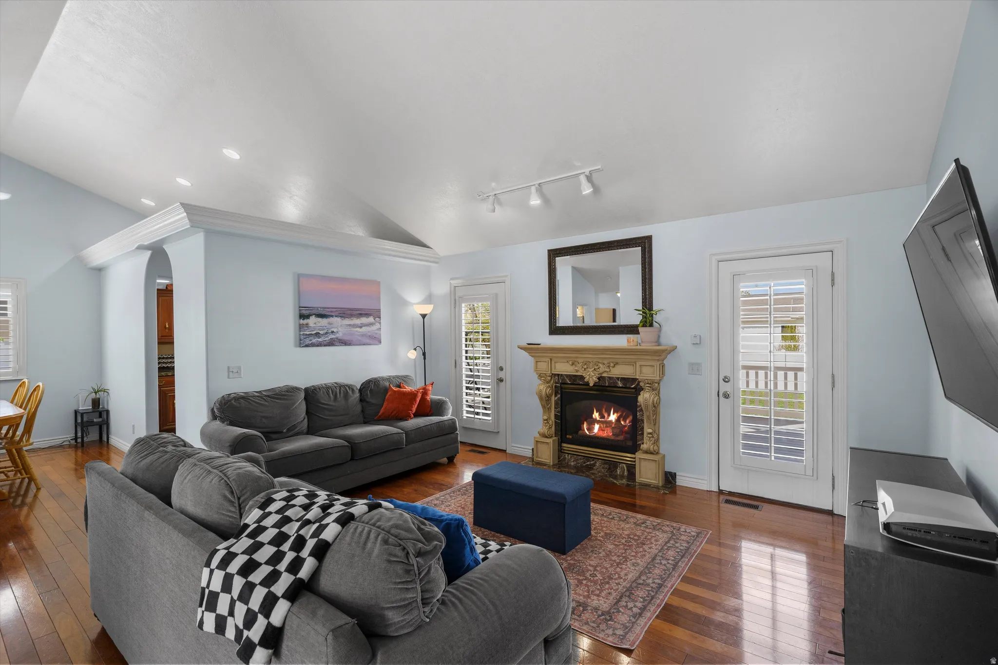 Living room with vaulted ceiling, dark wood flooring, arched walkways, plenty of natural light, and a premium fireplace