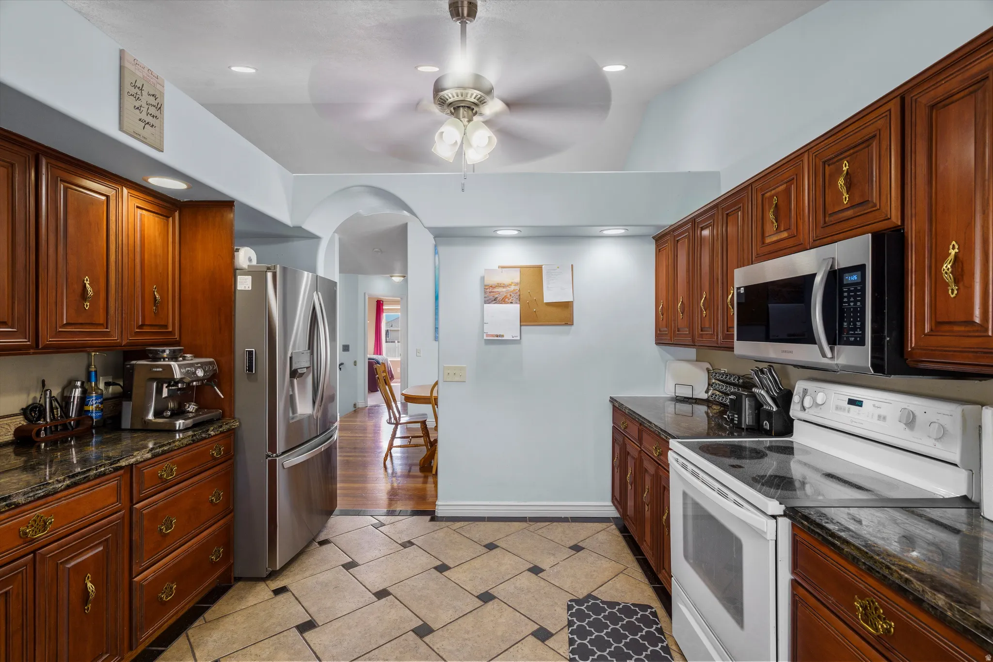 Kitchen with stainless steel appliances, dark stone countertops, a ceiling fan, recessed lighting, and light tile patterned flooring