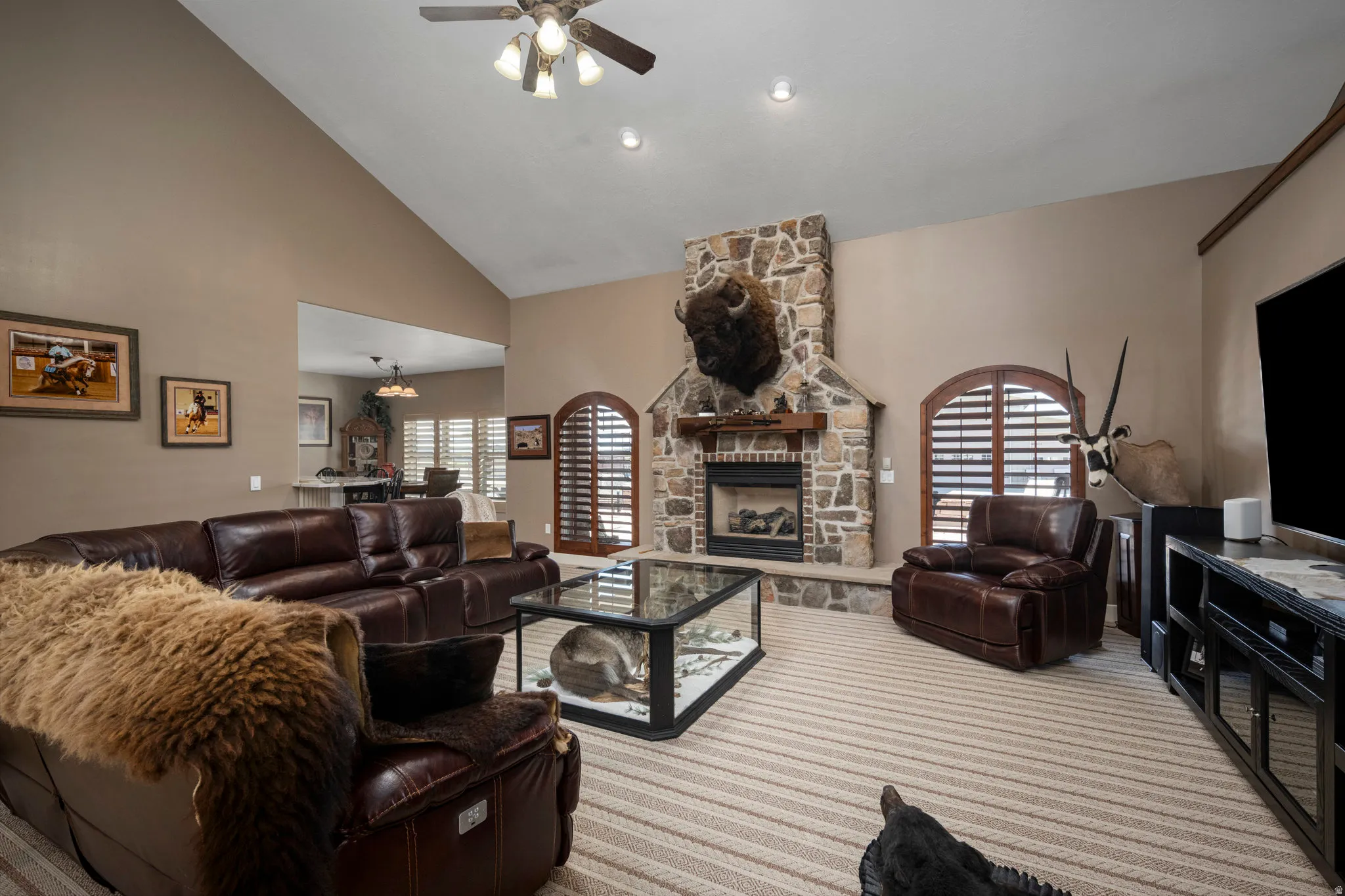 Carpeted living area featuring a ceiling fan, lofted ceiling, and a stone fireplace