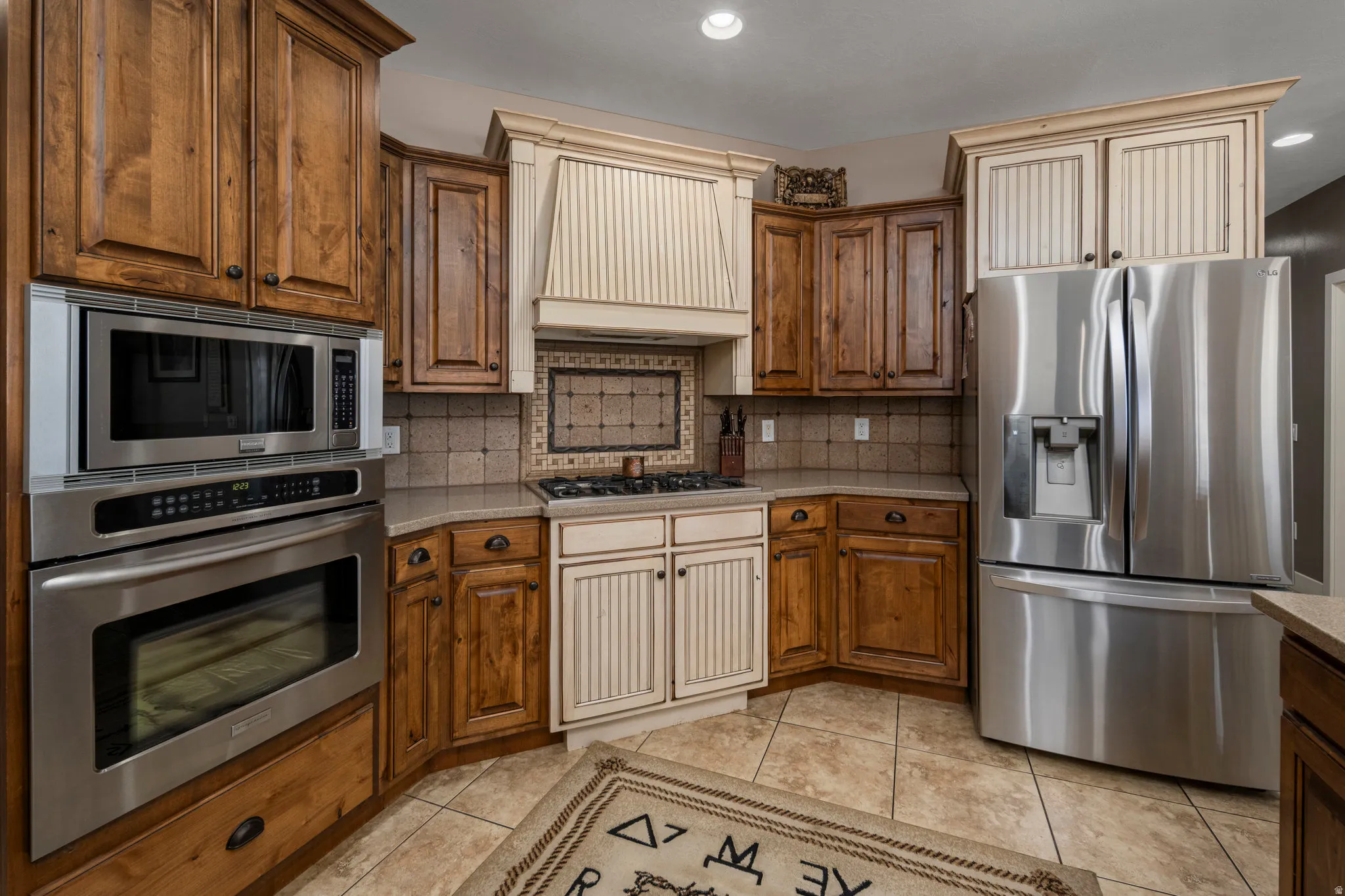 Kitchen featuring stainless steel appliances, tasteful backsplash, wood finish cabinets, light tile patterned flooring, and recessed lighting