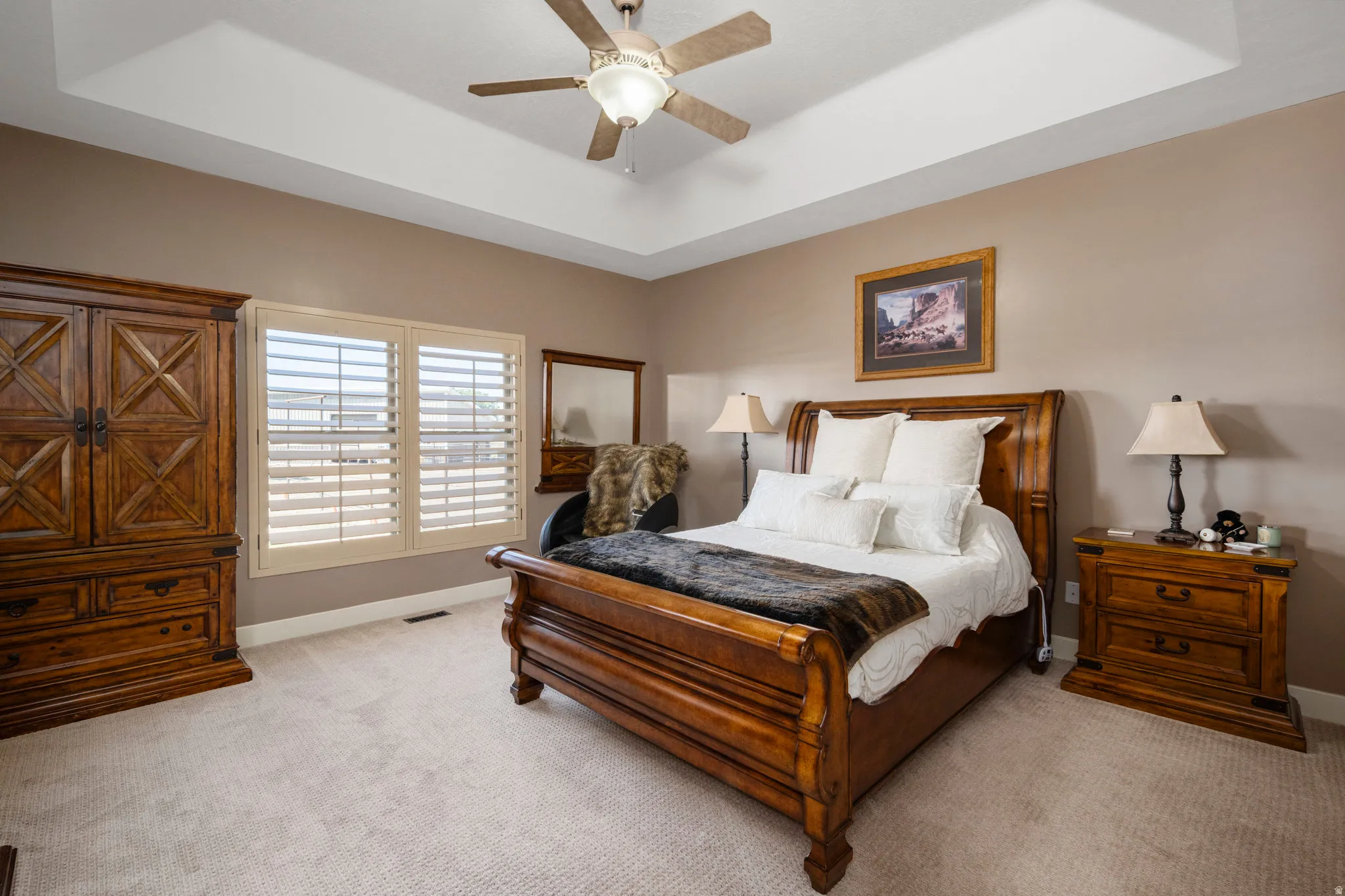 Bedroom featuring a tray ceiling, light carpet, and a ceiling fan