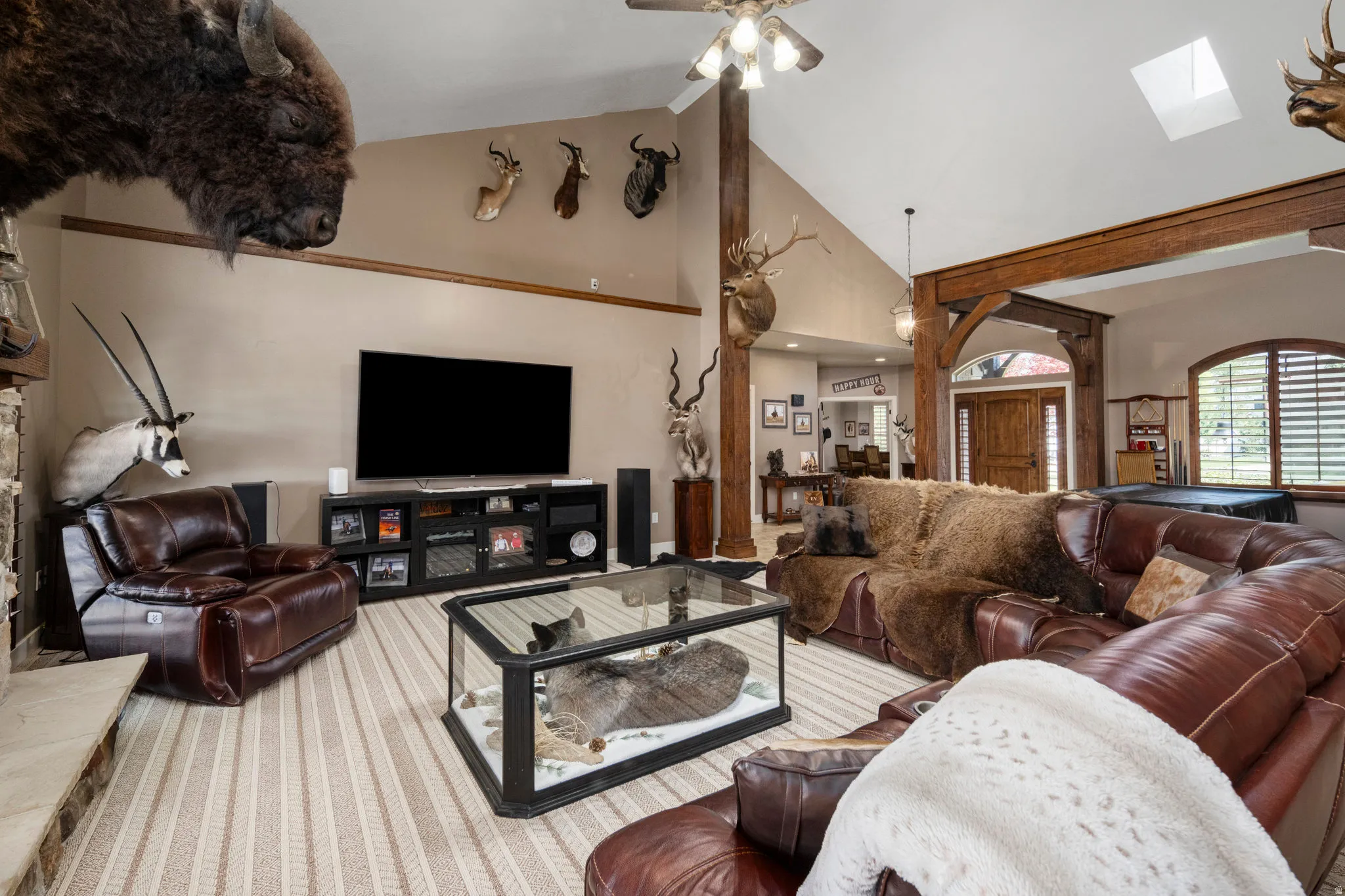 Living room featuring vaulted ceiling, ceiling fan, a fireplace with raised hearth, and a skylight