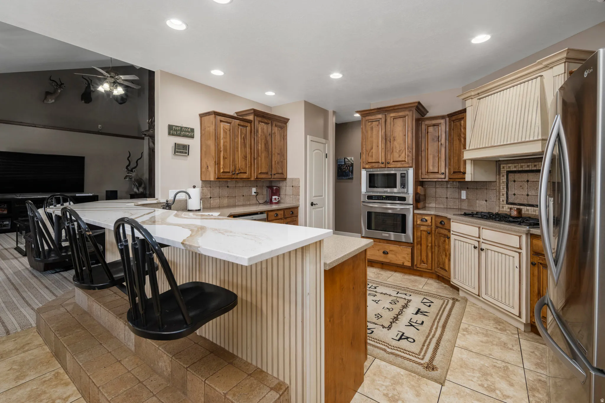 Kitchen featuring a peninsula, a breakfast bar area, stainless steel appliances, wood finish cabinets, and light stone countertops