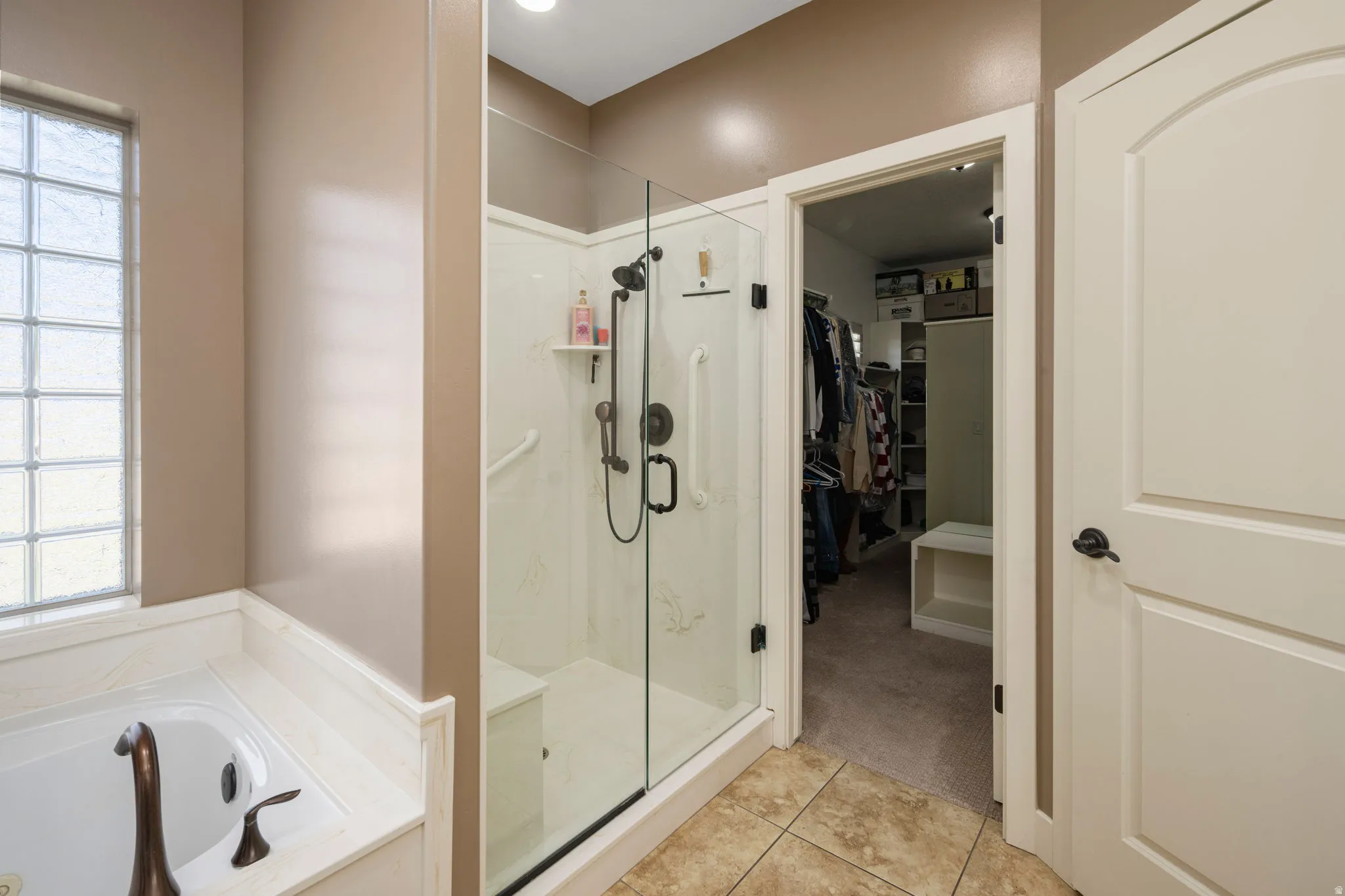 Full bath featuring a walk in closet, a bath, a shower stall, light colored carpet, and light tile patterned floors