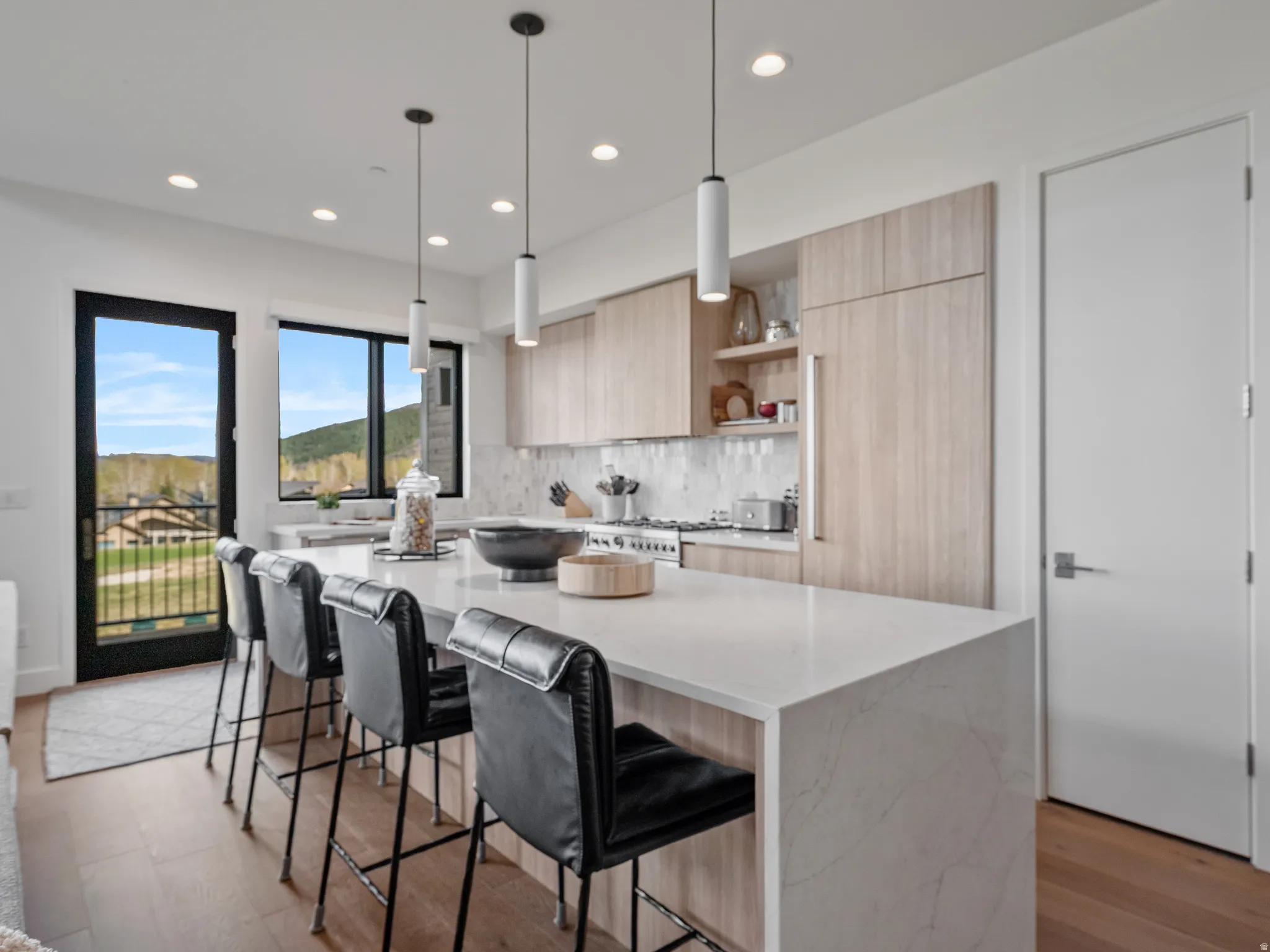 Kitchen featuring light wood finish cabinetry, modern cabinets, a kitchen bar, open shelves, and hanging light fixtures