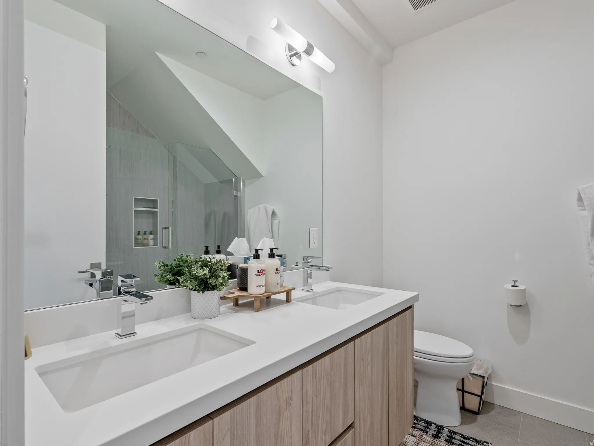 Bathroom with double vanity, light tile patterned floors, and a shower with door