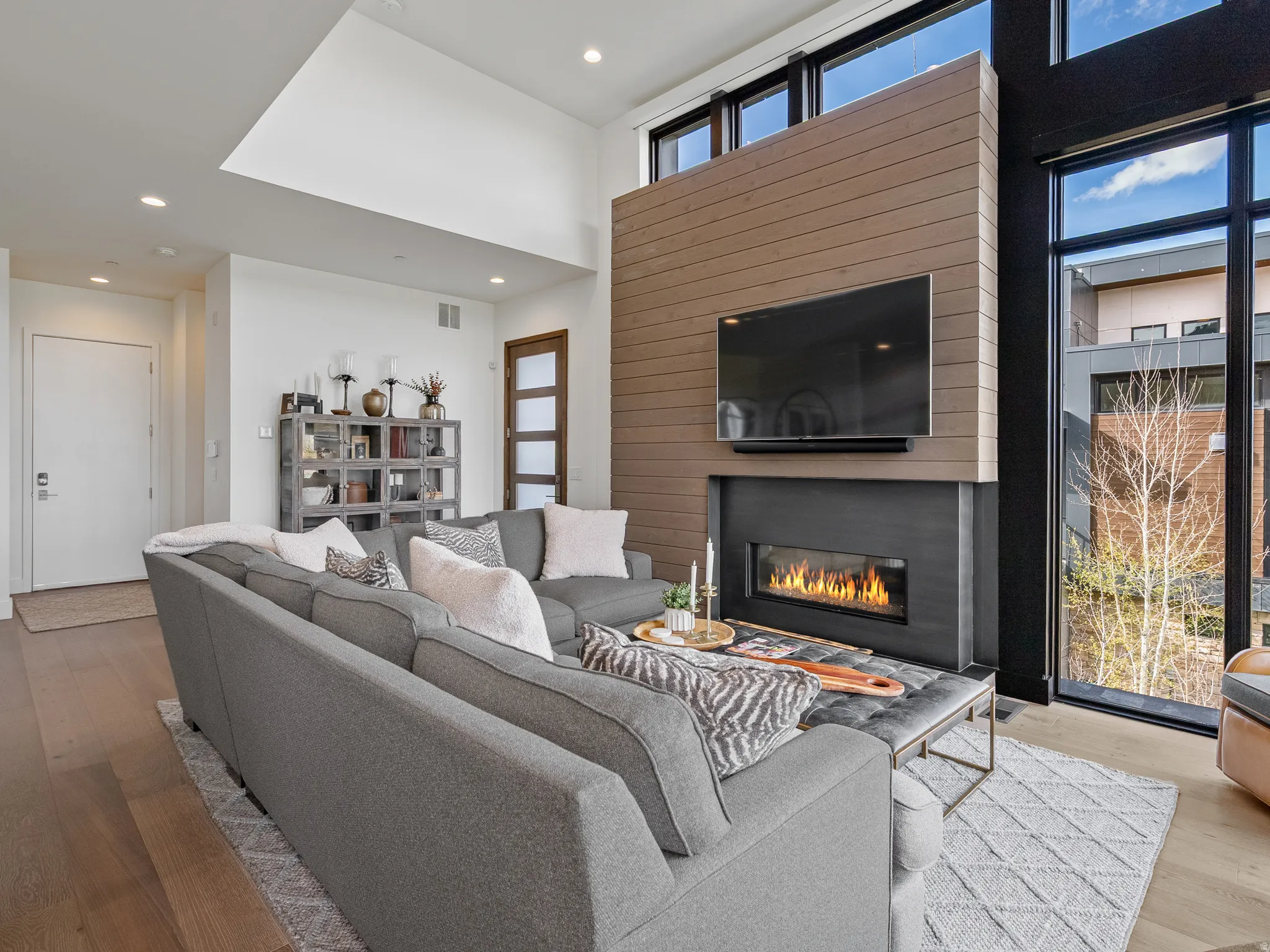 Living room with hardwood / wood-style floors, a high ceiling, a glass covered fireplace, and recessed lighting