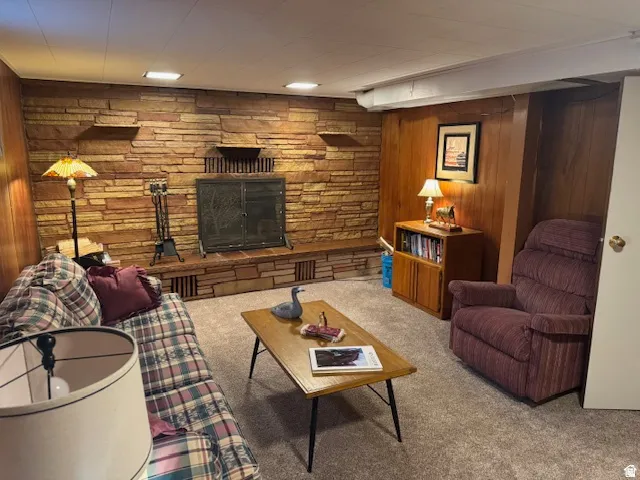 Carpeted living room featuring wood walls and a stone fireplace