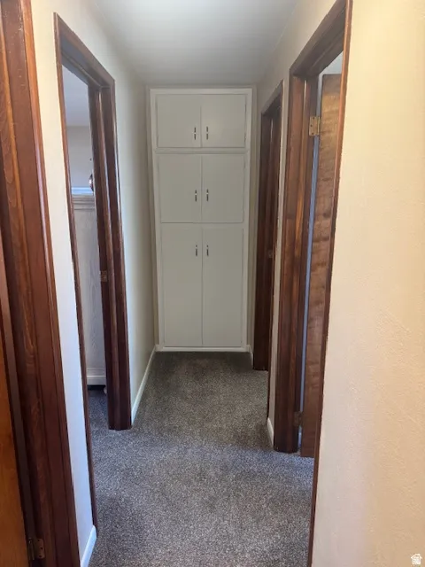 Hallway featuring dark carpet and baseboards