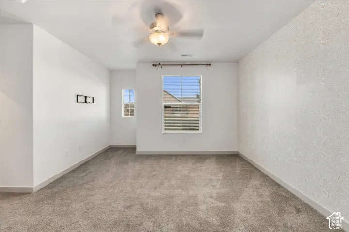 Textured accent wall, ceiling fan with integrated lighting, two windows with blinds, and neutral carpet flooring
