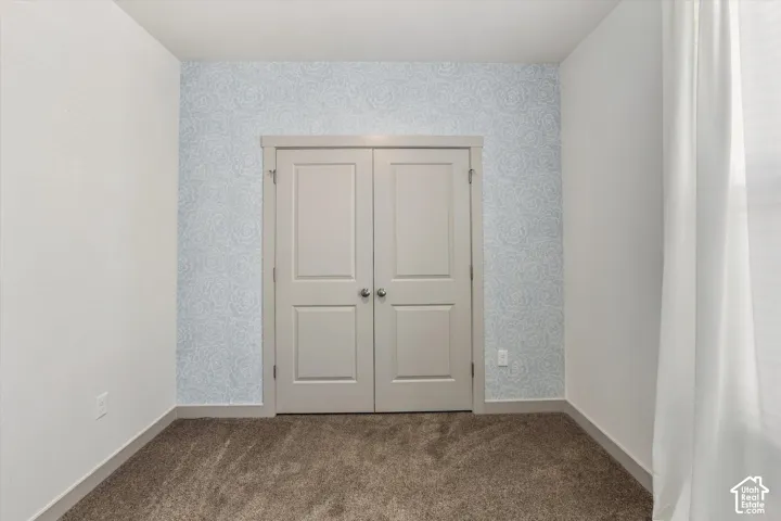 Light-toned carpeting, patterned accent wall, white painted walls, and double panel doors with silver-tone hardware