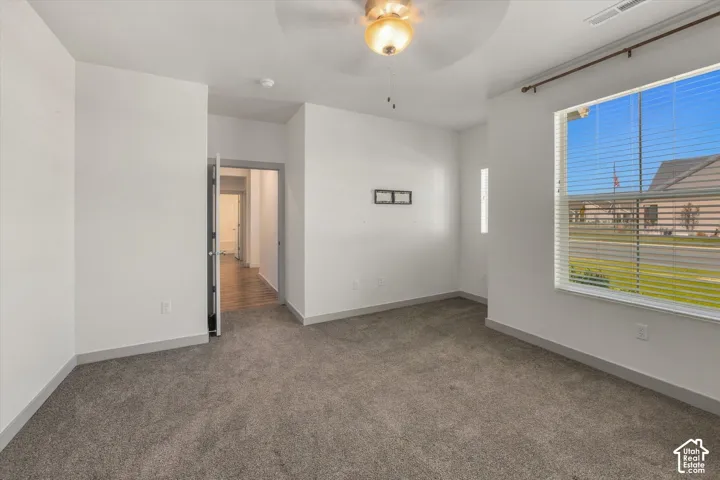Spacious room featuring neutral carpeting, a built-in ceiling fan, window blinds, and a tray ceiling