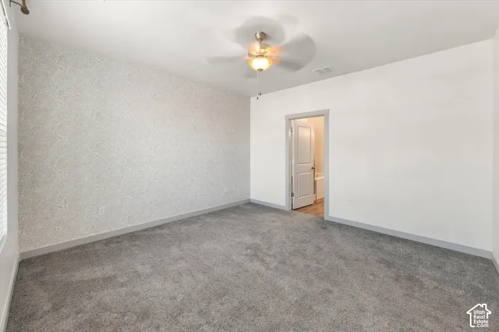 Plush gray carpeting, patterned accent wall, ceiling fan with integrated lighting, and gray trim