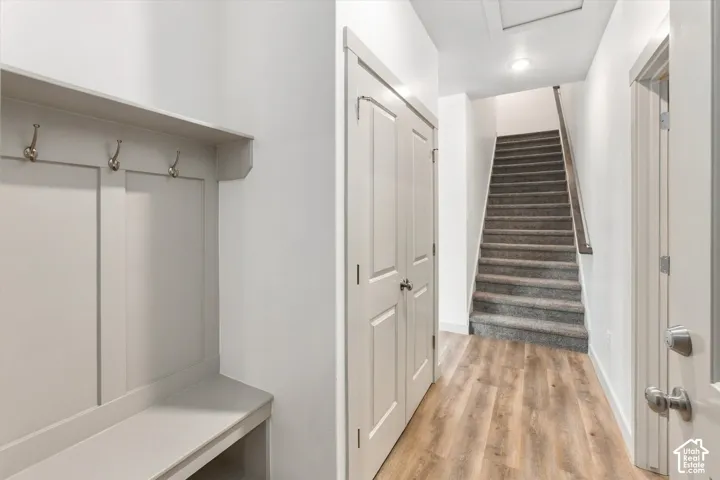 Built-in storage bench with coat hooks, wood-finish flooring, white paneled doors, and carpeted staircase