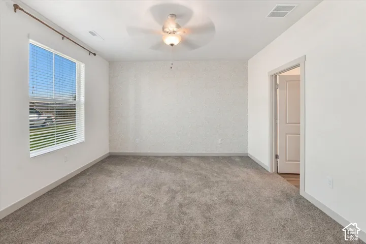 Neutral gray carpeting, white painted walls, and a ceiling fan with integrated lighting