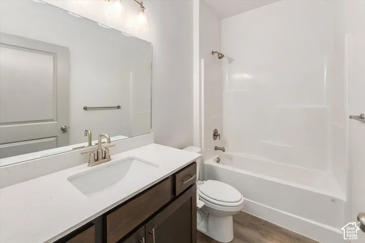 Bathroom featuring a white integrated sink, dark wood-finish vanity with brushed nickel hardware, expansive vanity mirror, and a white tub/shower combination